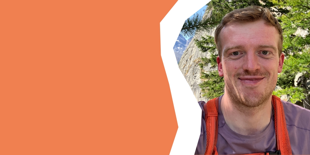 Ali smiling to camera whilst walking through a mountainous landscape on a hot, sunny summers' day