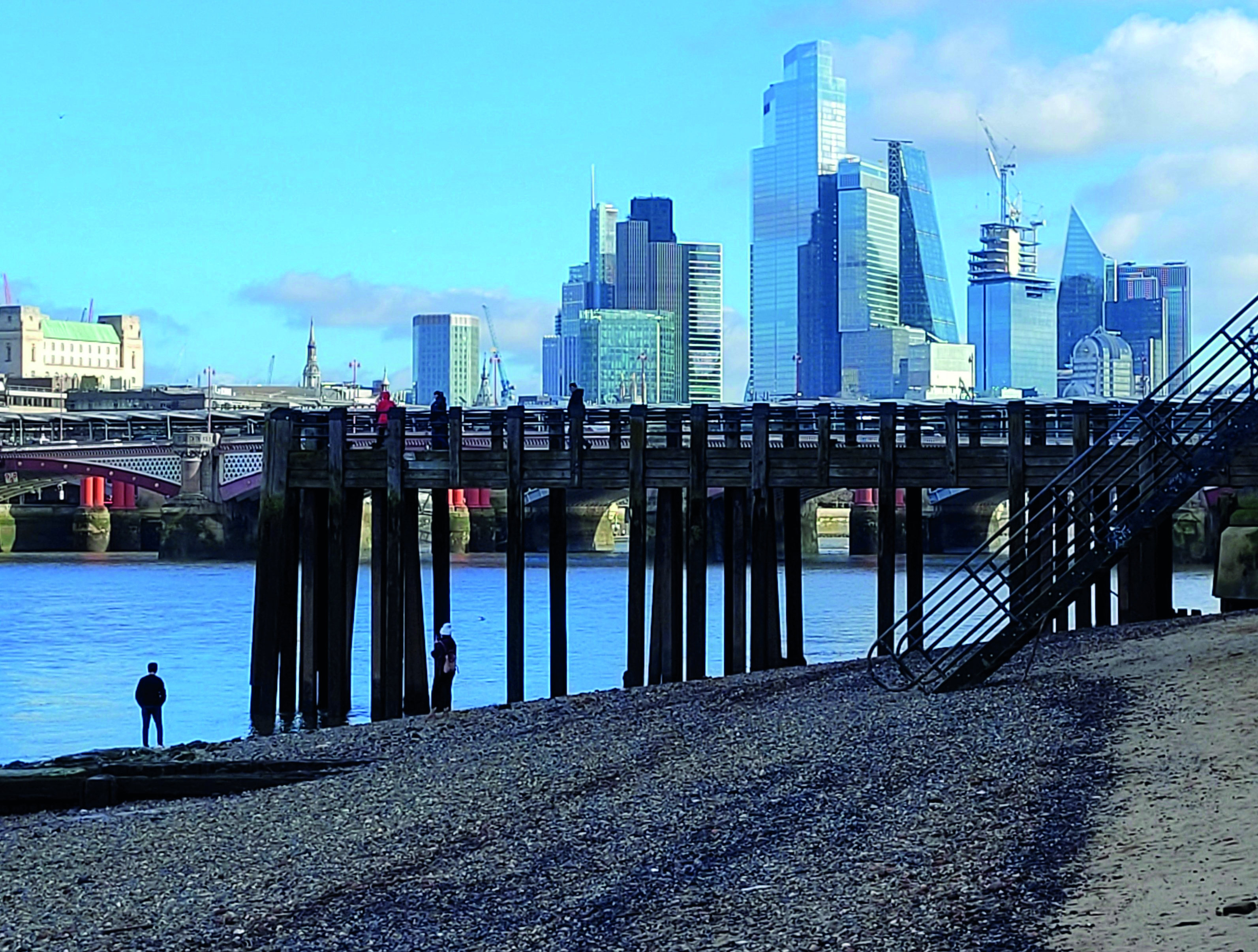 View of London from the banks of the Thames on a bright sunny day. The view looks east towards the City, with skyscrapers across the shoreline 