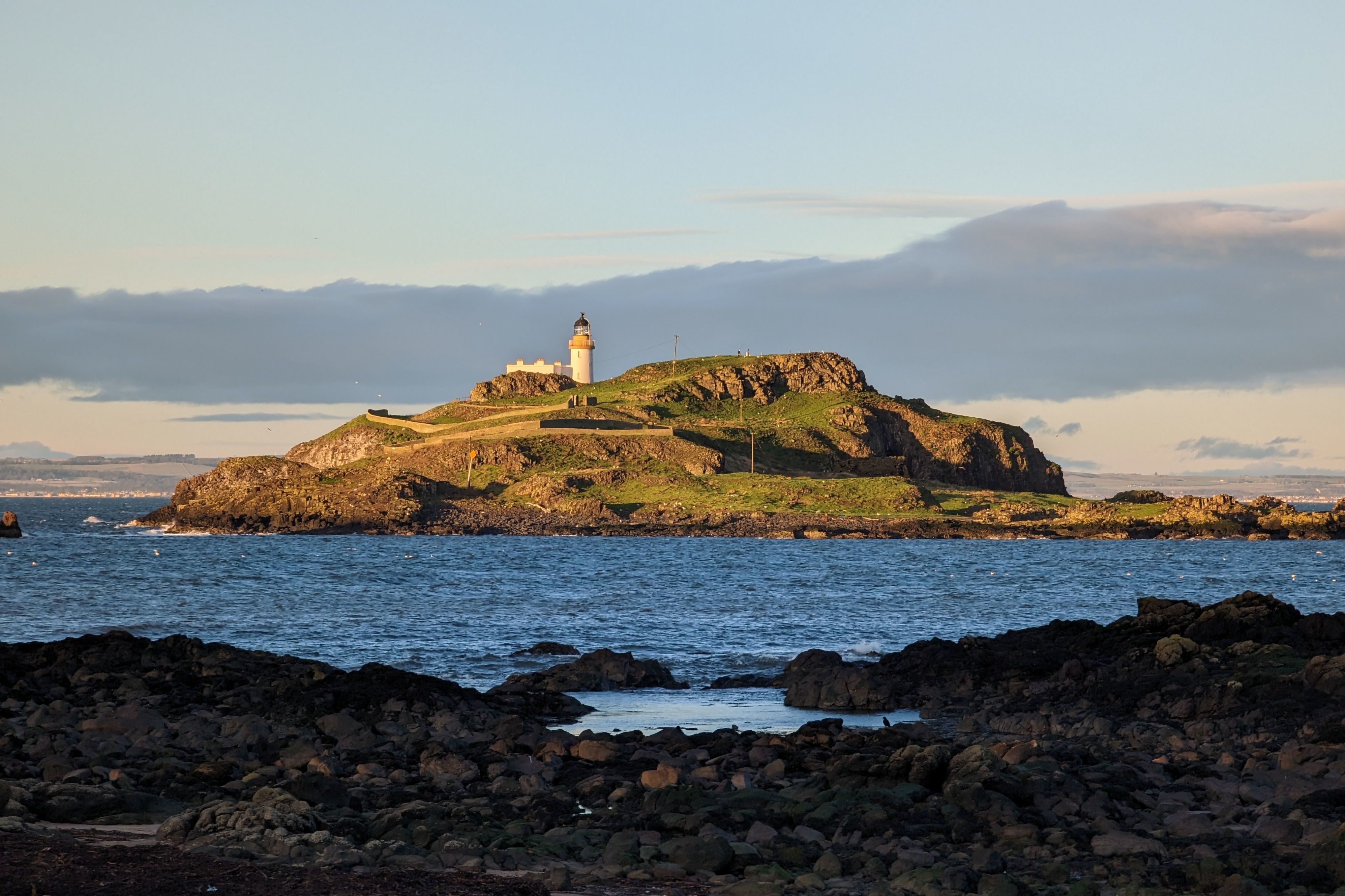 A lighthouse stands atop a small, rocky island off the Scottish coast