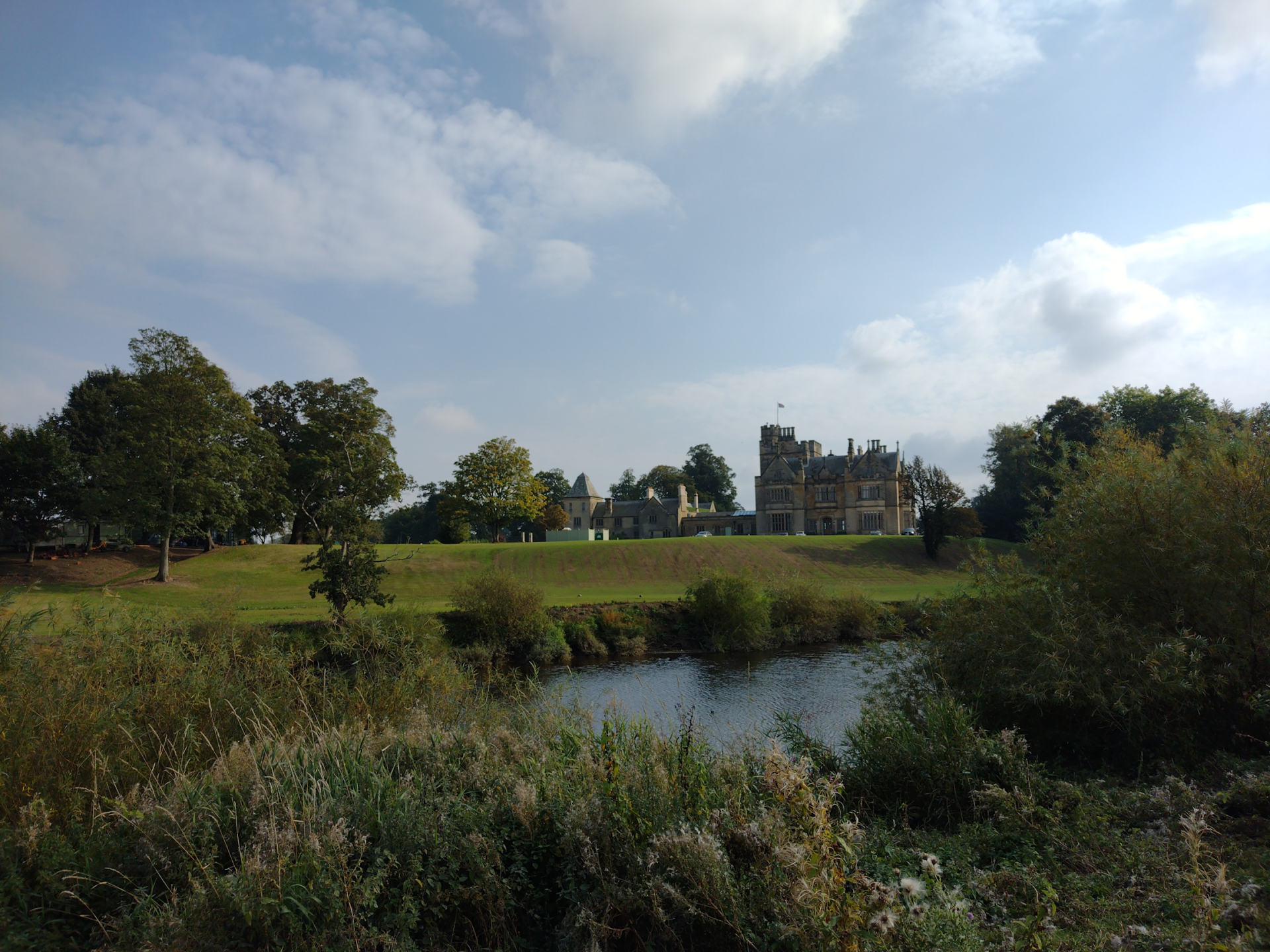 The image is of a river scene with a large, grand house visible amongst the grass and trees on the opposite bank.