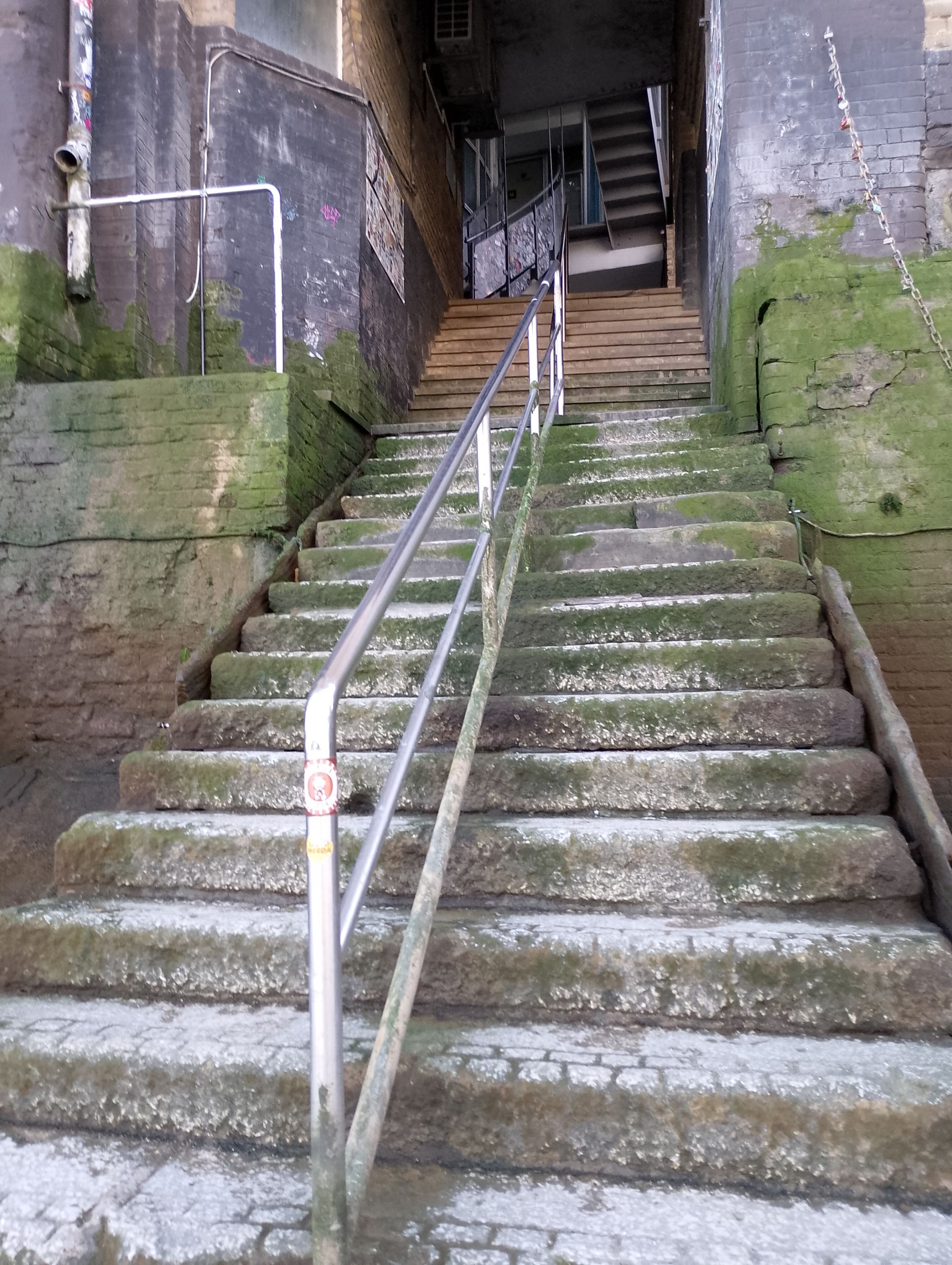 A set of ageing concrete steps with a metal rail down the middle. Photo taking an upward shot from the bottom.