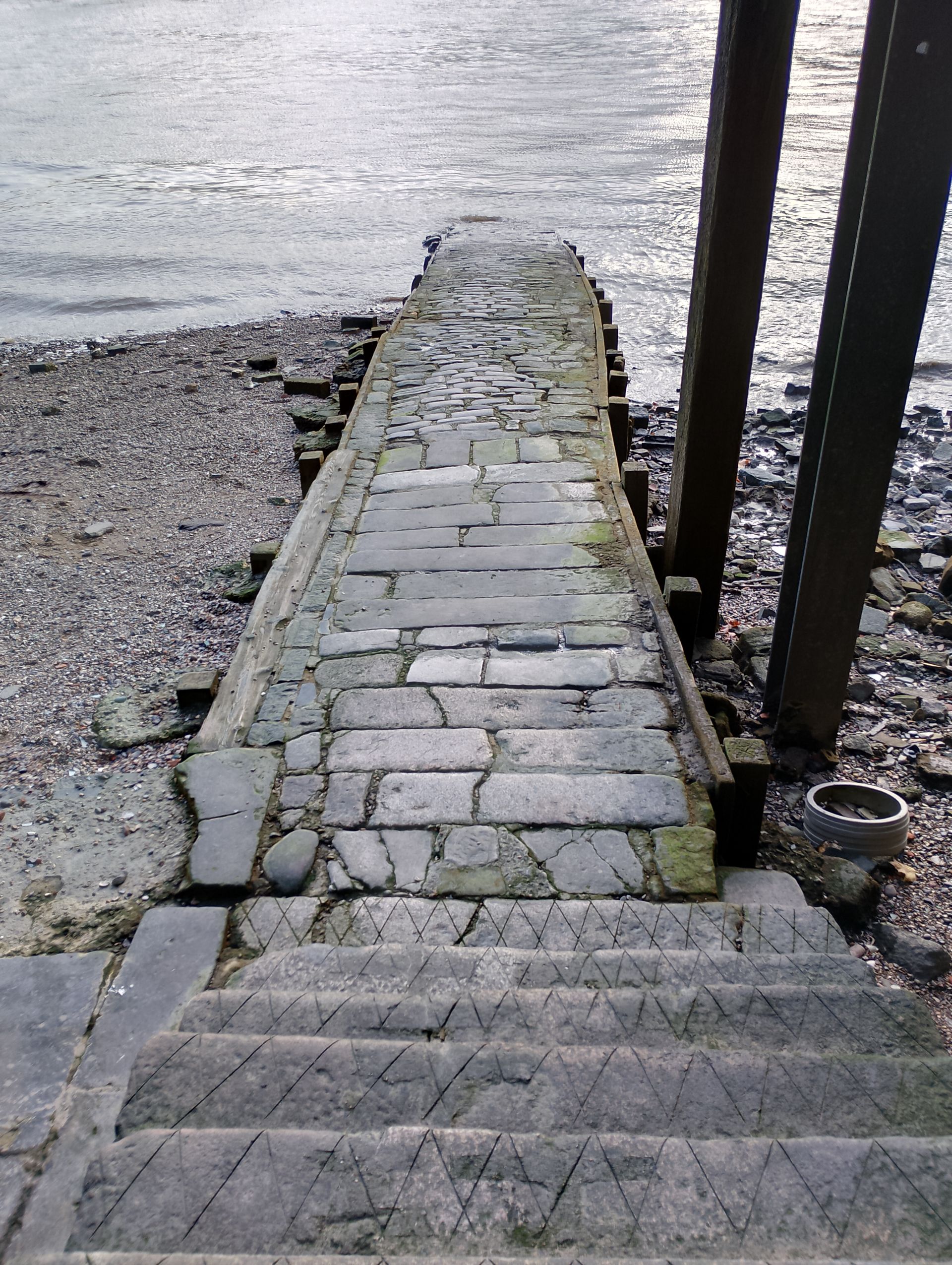 Looking down a set of ageing concrete steps leading to a path slightly submerged in river water.