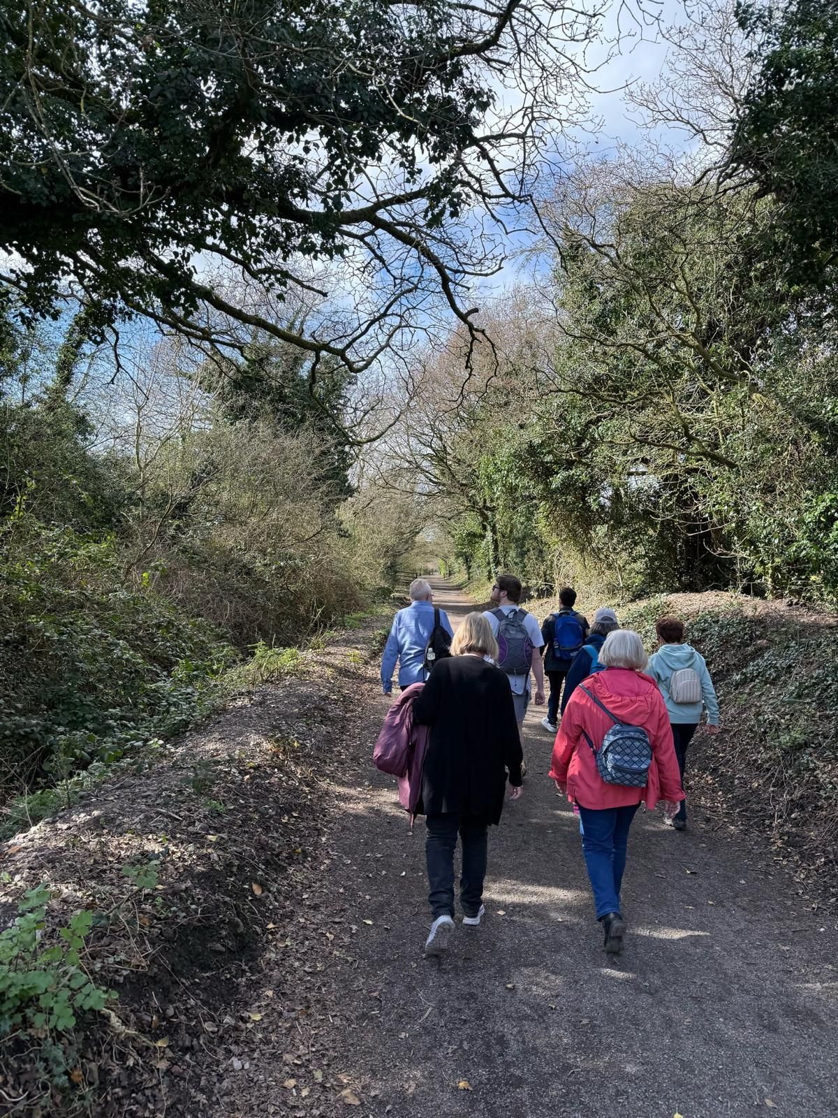 A group of people walking along a surfaced path with embankments and greenspace on either side
