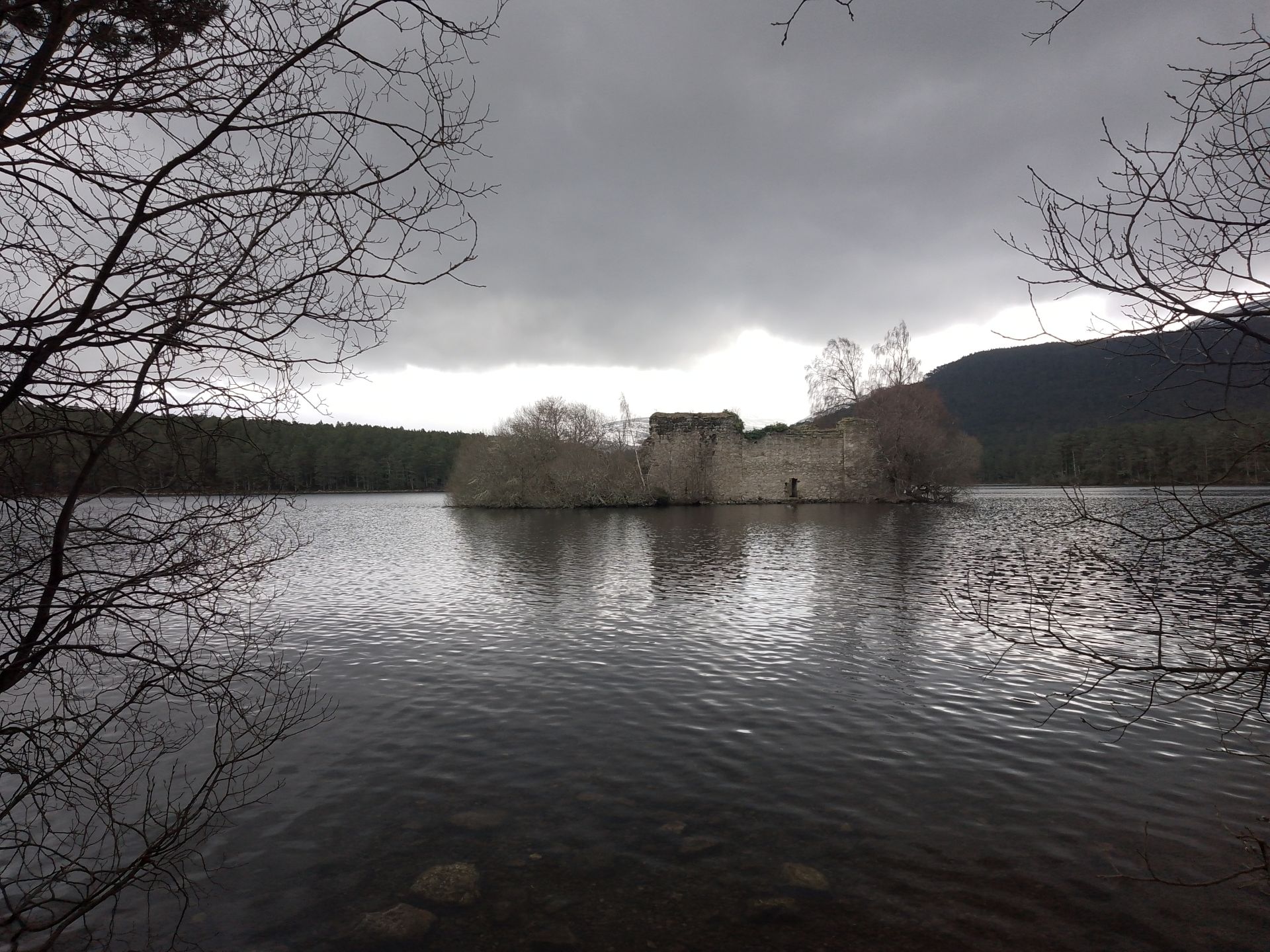 View of castle ruin on loch with grey sky