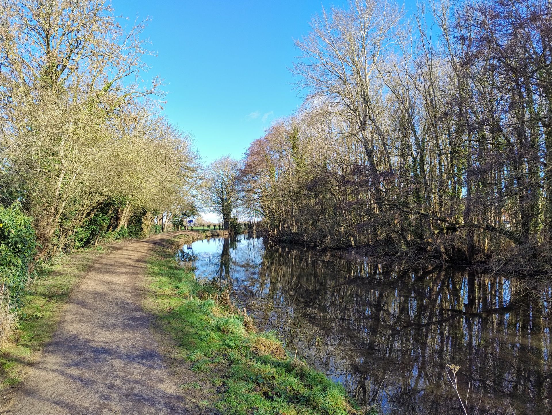 View along a curving tree lined canal path on a sunny spring day