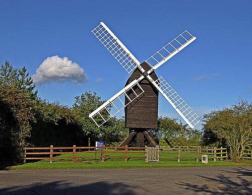 Gransden Mill a post mill surrounded by trees and backed by brilliant blue sky and a single cloud