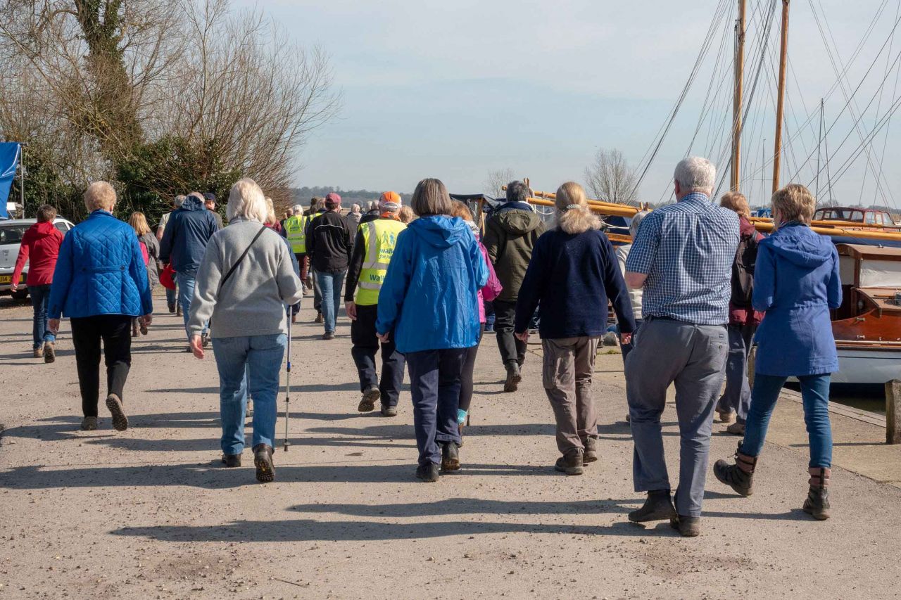 walkers on a shore line next to moored boats