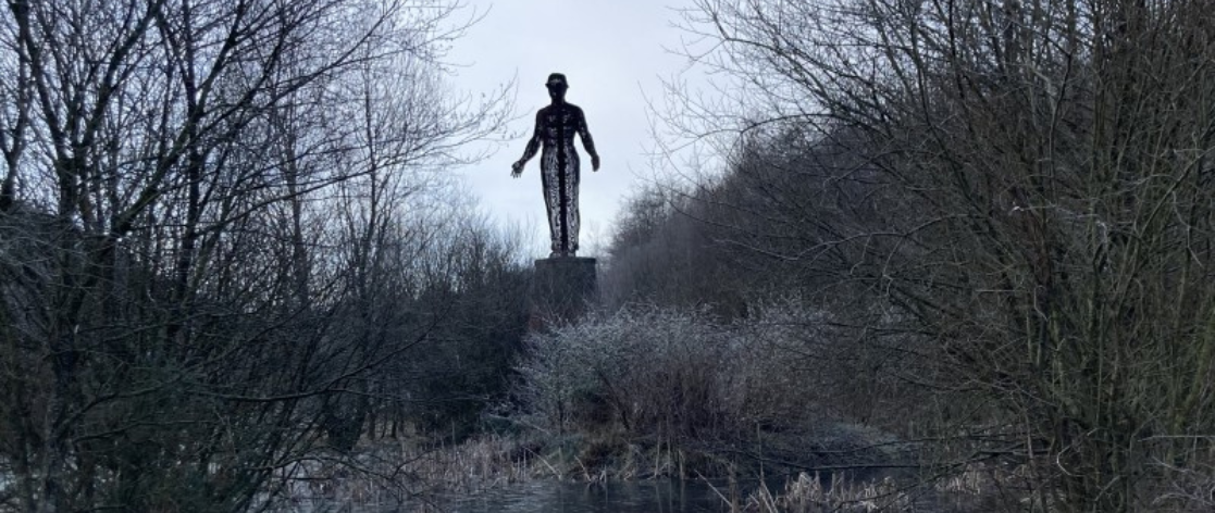 A large statue of a man looms over wintry woodland