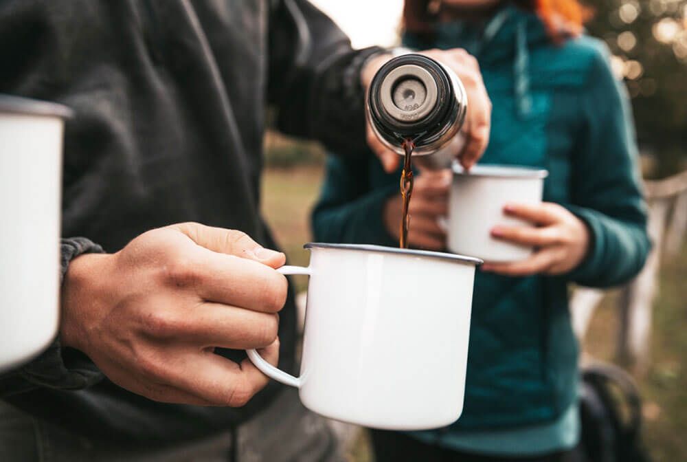 Someone pouring tea from a flask into camping mug, outside