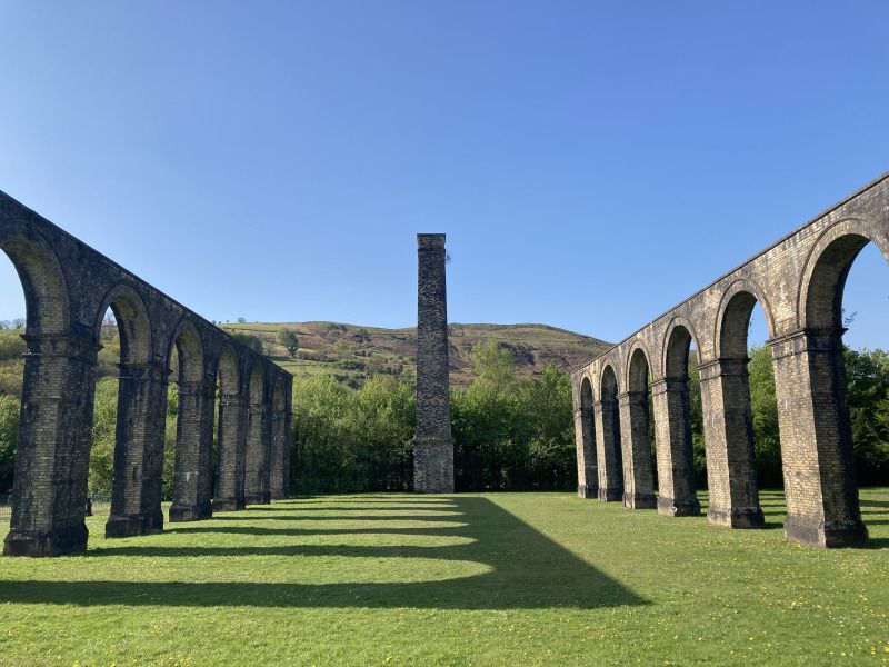 An abandoned aqueduct stands in front of a tall chimney