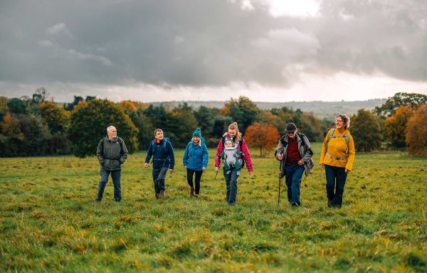 A group of six Ramblers walking across a field with woodland behind them