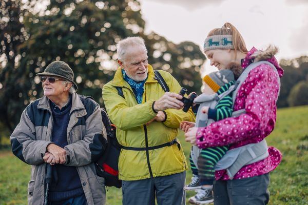 Women wearing a baby carrier on a group walk. Man showing baby his binoculars.