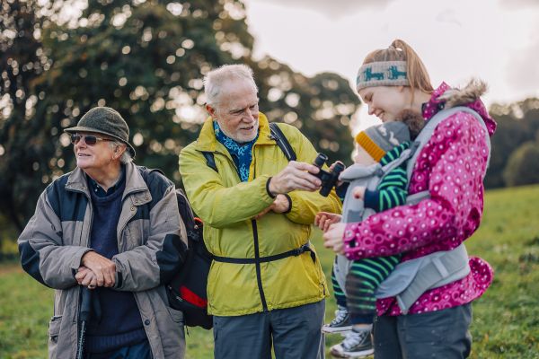 Women wearing a baby carrier on a group walk. Man showing baby his binoculars. 