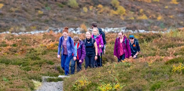 A group of seven young hikers following a narrow path across moorland