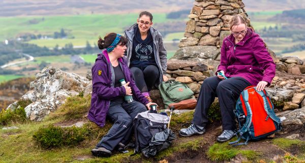 Three women sitting on rocks, wearing different styles of trousers