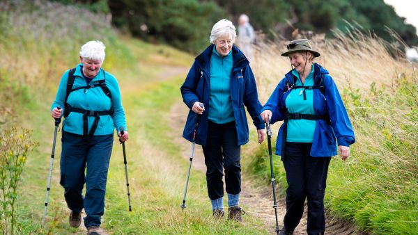 Three women walking down a path each using walking poles