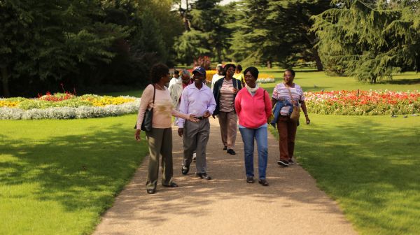 A group of people walking along a path in a local park with grass, trees and flowers