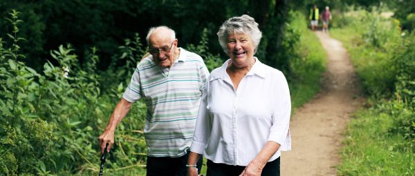 A man walking with a walking stick with a lady by his side