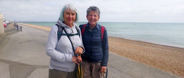 Two women standing on a boardwalk in front of a shingle beach