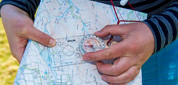 A close up of someone's hands holding a compass on a map