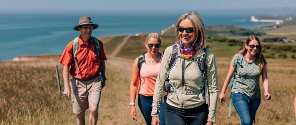 Four people walking along a grassy path above a cliff