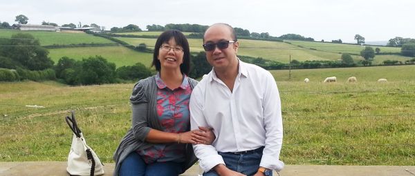 A woman and man sitting on a wall in front of a grassy field