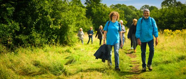 Two walkers, both wearing light blue, lead a group down a grassy path.