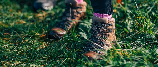 A close up of a pair of brown walking boots, standing in short, wild grass