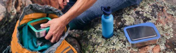 Person putting container into backpack, outside. 