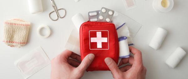 Hands picking up first aid travel kit bag for emergency on white table.
