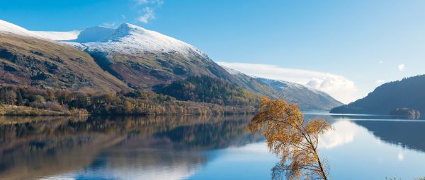 A snow topped Helvellyn mountain viewed from a clear Thirlmere water in Autumn