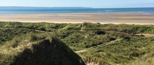 An area of sand dune leading to a wide flat beach then the sea