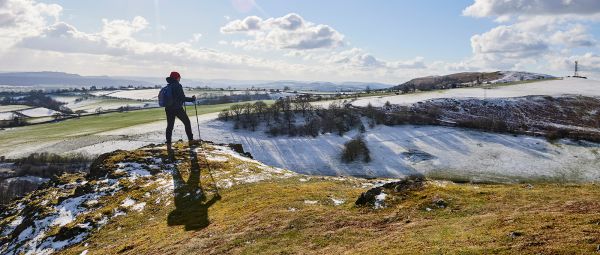 A woman standing upon a hill, looking out at a snowy view of hills