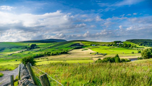 A lush sweeping expanse of fields cover rolling hills under a cloudy sky