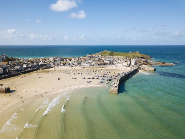 The wide beach at St Ives runs between the twin sea walls and toward the main town, with the headland and sea beyond.