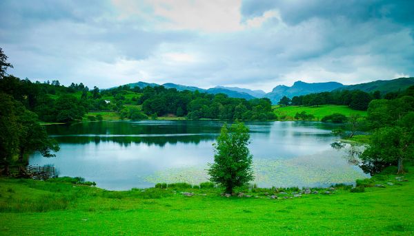 A tranquil lake surrounded by green hills with mountains in the distance