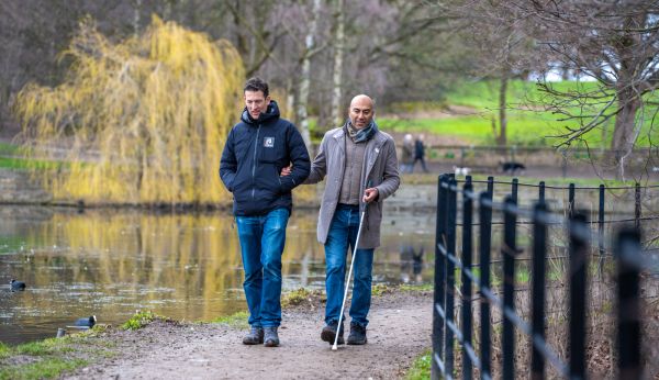 Amar Latif, the blind adventurer and president of the Ramblers, being guided on a path alongside a lake.