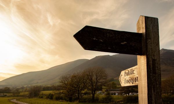 A waymark showing public footpath ahead with rolling hills in the background.