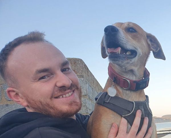 A rambler smiling into the camera holding his dog who is looking into the distance