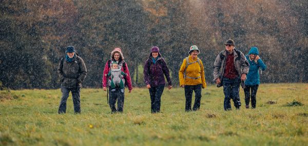 Six walkers in a rainy field, one carrying a baby