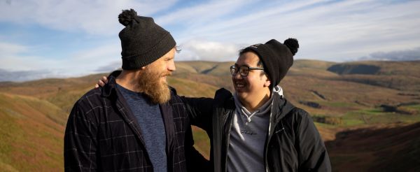 Two walkers standing in an embrace with rolling hills behind them