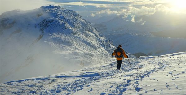 walker on snowcapped mountains using poles and carrying a backpack