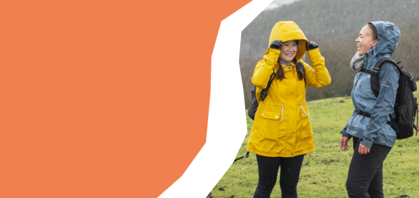 two smiling walkers in waterproof jackets and carrying a backpacks in the rain