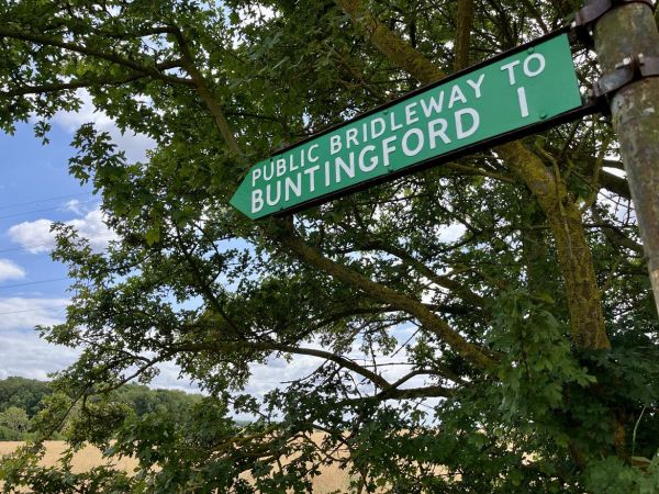A bridleway fingerpost against a tree and arable landscape