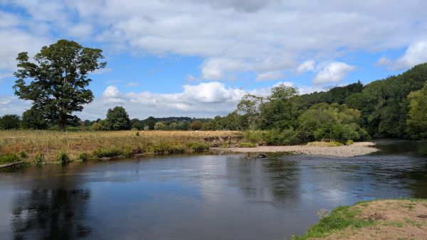 River Dee reflecting blue sky and cloudes, with trees and fields visible on the far bank