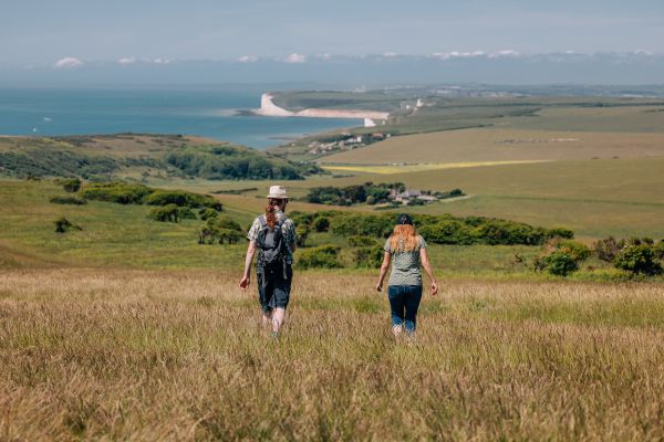 Two walkers make their way down hill as a coastal landscape fills the horizon