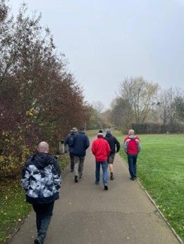 A cloudy but dry picture of 6 men walking on a pavement through a park.