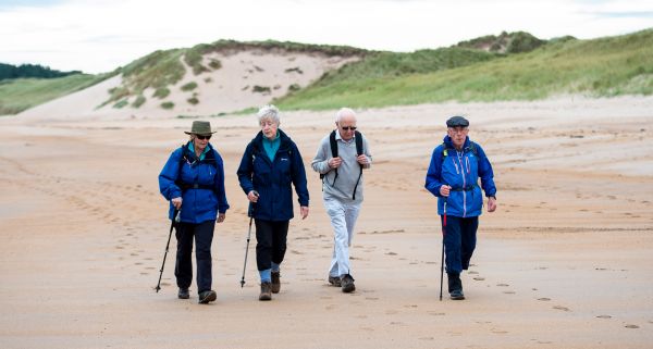 A group of four older walkers make their way down a wide, sandy beach