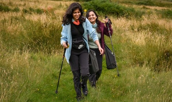 Two young woman walking with poles through long grass