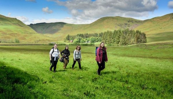 Young women walking in a lush green field with grassy hills behind